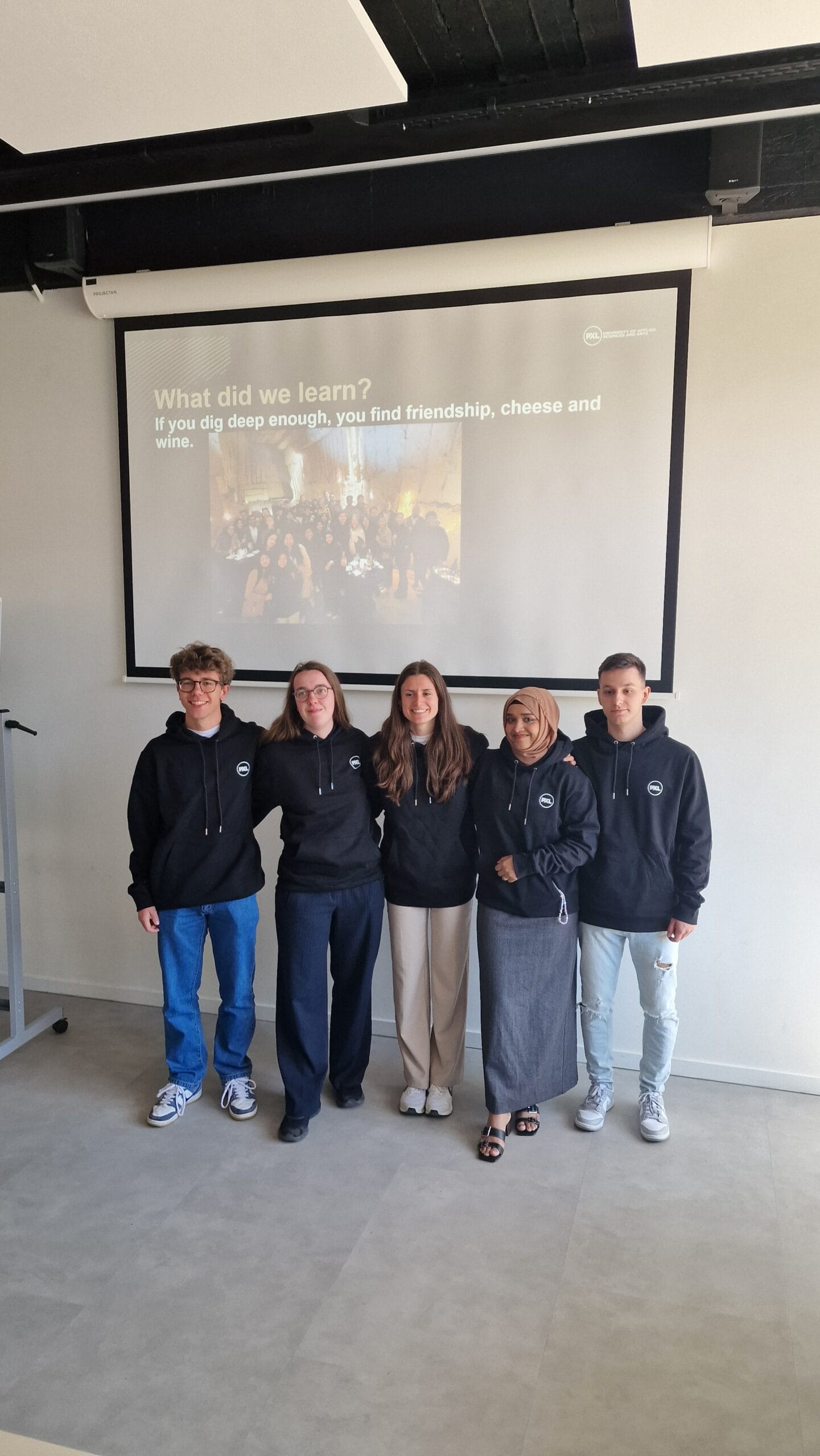 Diverse university students in black hoodies at a workshop or presentation event.